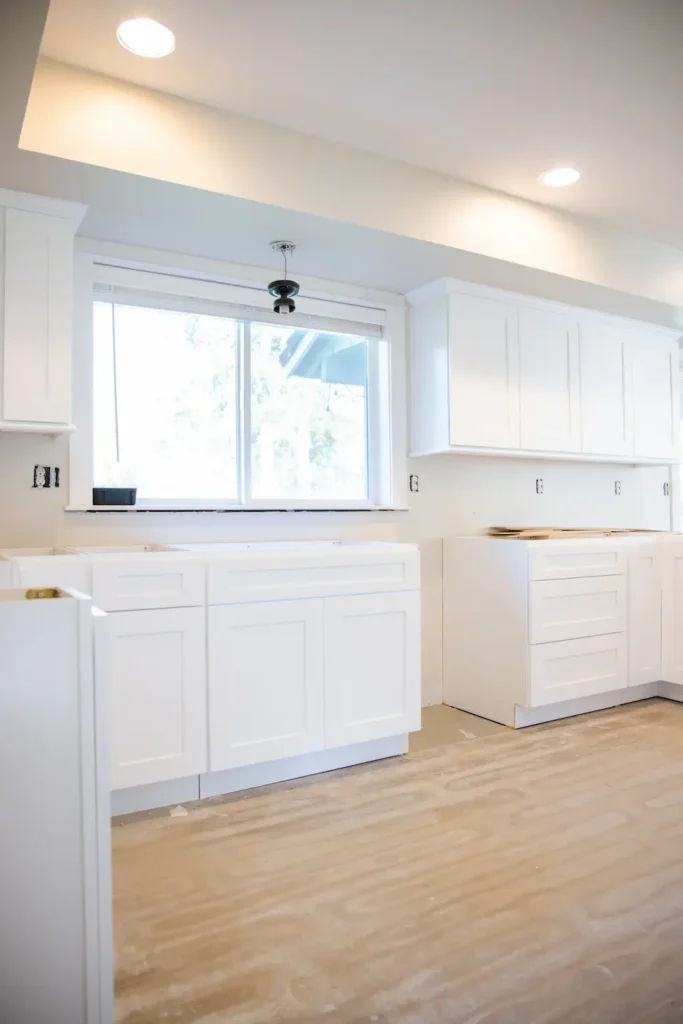 Kitchen with white cabinets, light wood floor, large window, and recessed lights.